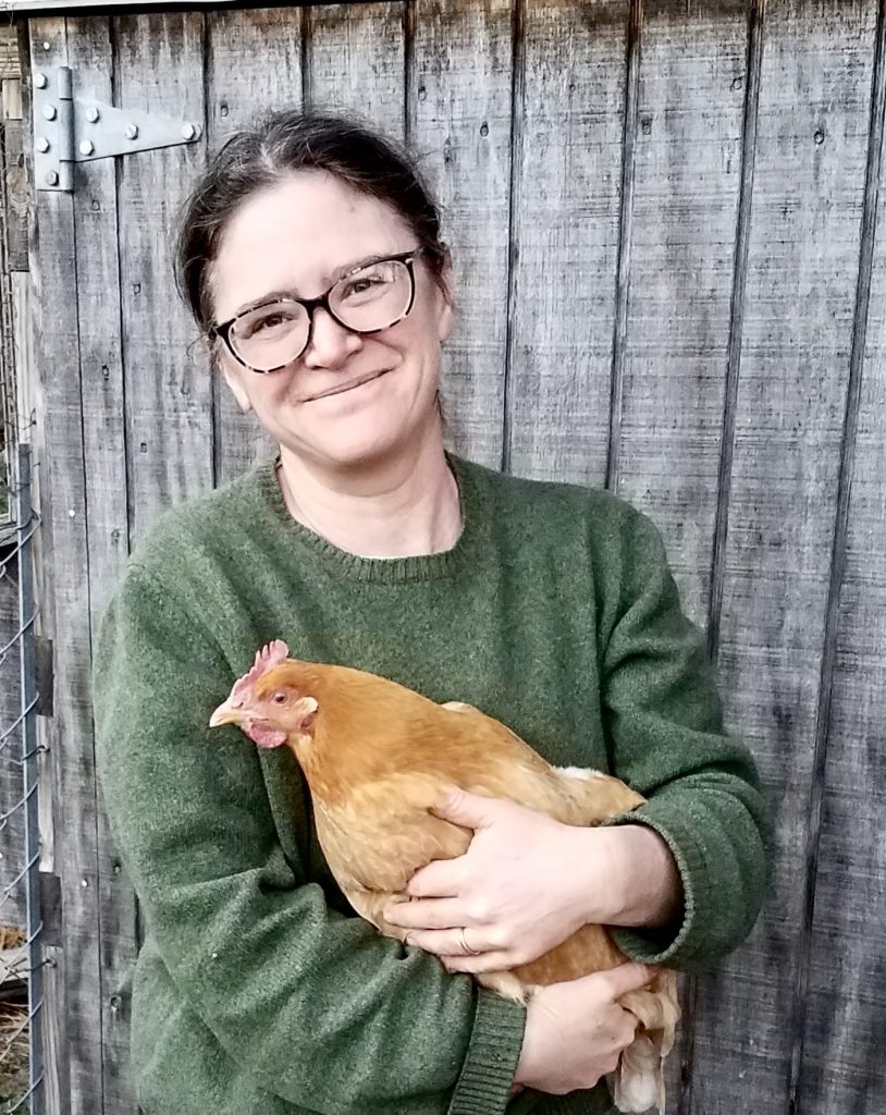 Sara holds a chicken and smiles into the camera