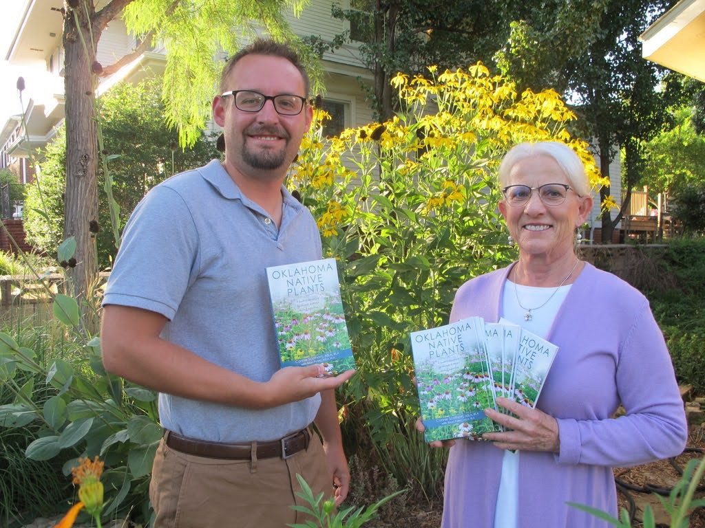Two people smile at the camera and hold a book titled "Oklahoma Native Plants"